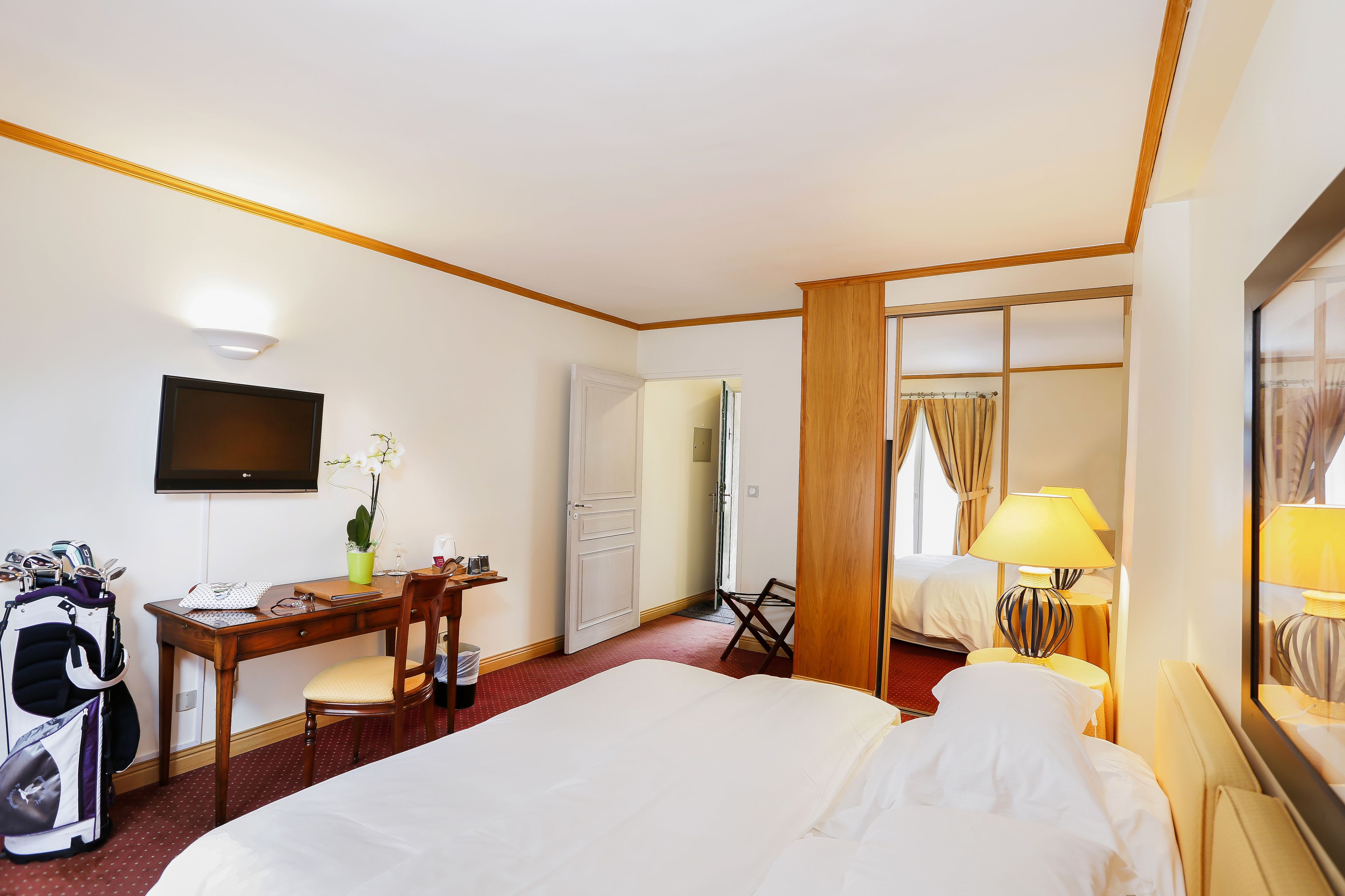 Una habitación de hotel con cama, escritorio, silla, televisión y un bolso de golf.