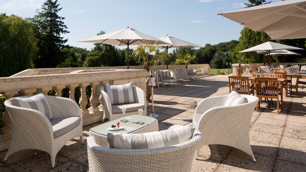 An outdoor patio area with wicker furniture, umbrellas, and a stone balustrade. - Domaine et Golf de Vaugouard - La Maison Younan (Fontenay-sur-Loing)