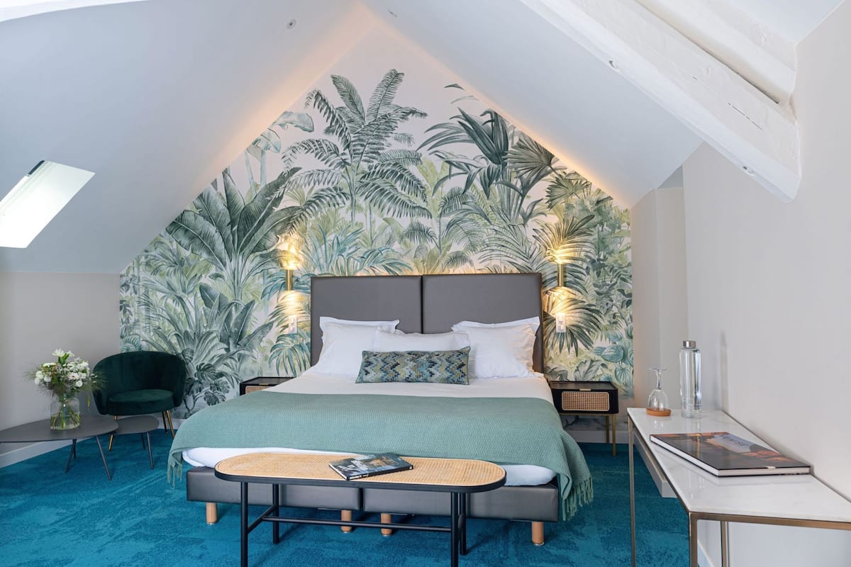Un dormitorio con una cama grande, un escritorio, una silla y un papel tapiz tropical.