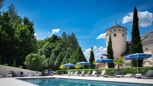 A swimming pool with lounge chairs and umbrellas, surrounded by trees and a tower. - Domaine et Golf de Vaugouard - La Maison Younan (Fontenay-sur-Loing)
