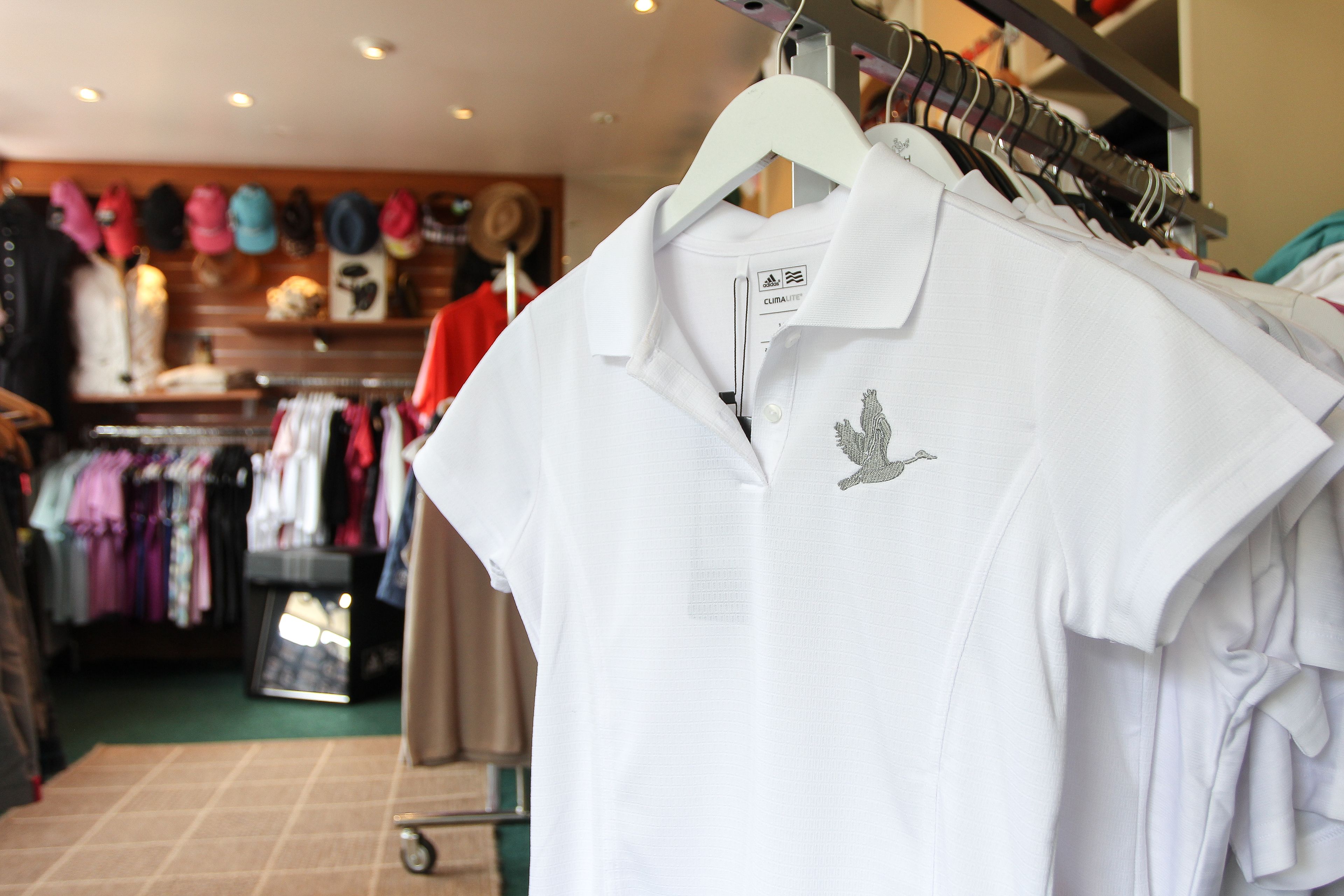 A clothing store with racks of white polo shirts and hats.