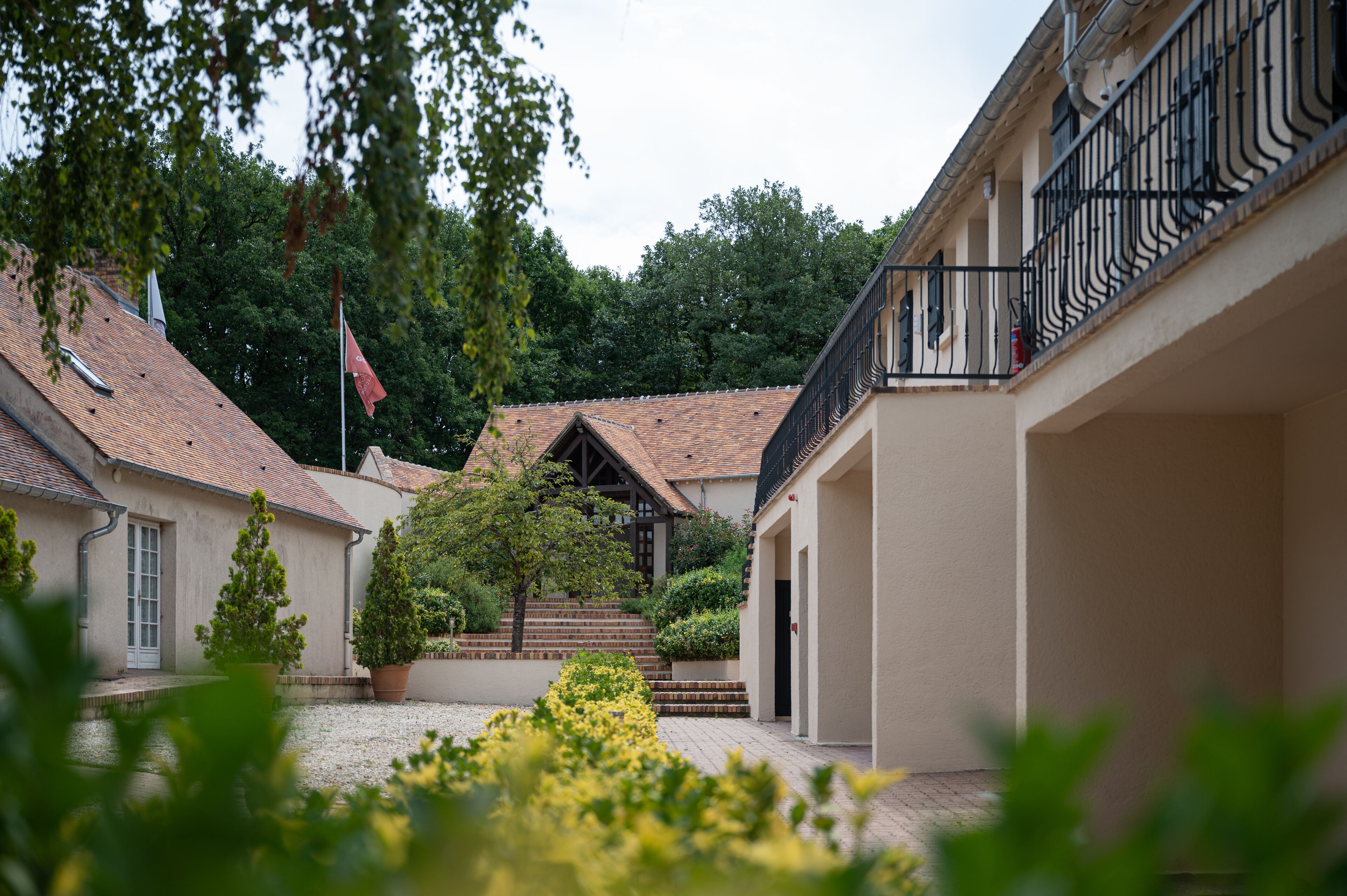A courtyard with buildings, a flag, and potted plants.
