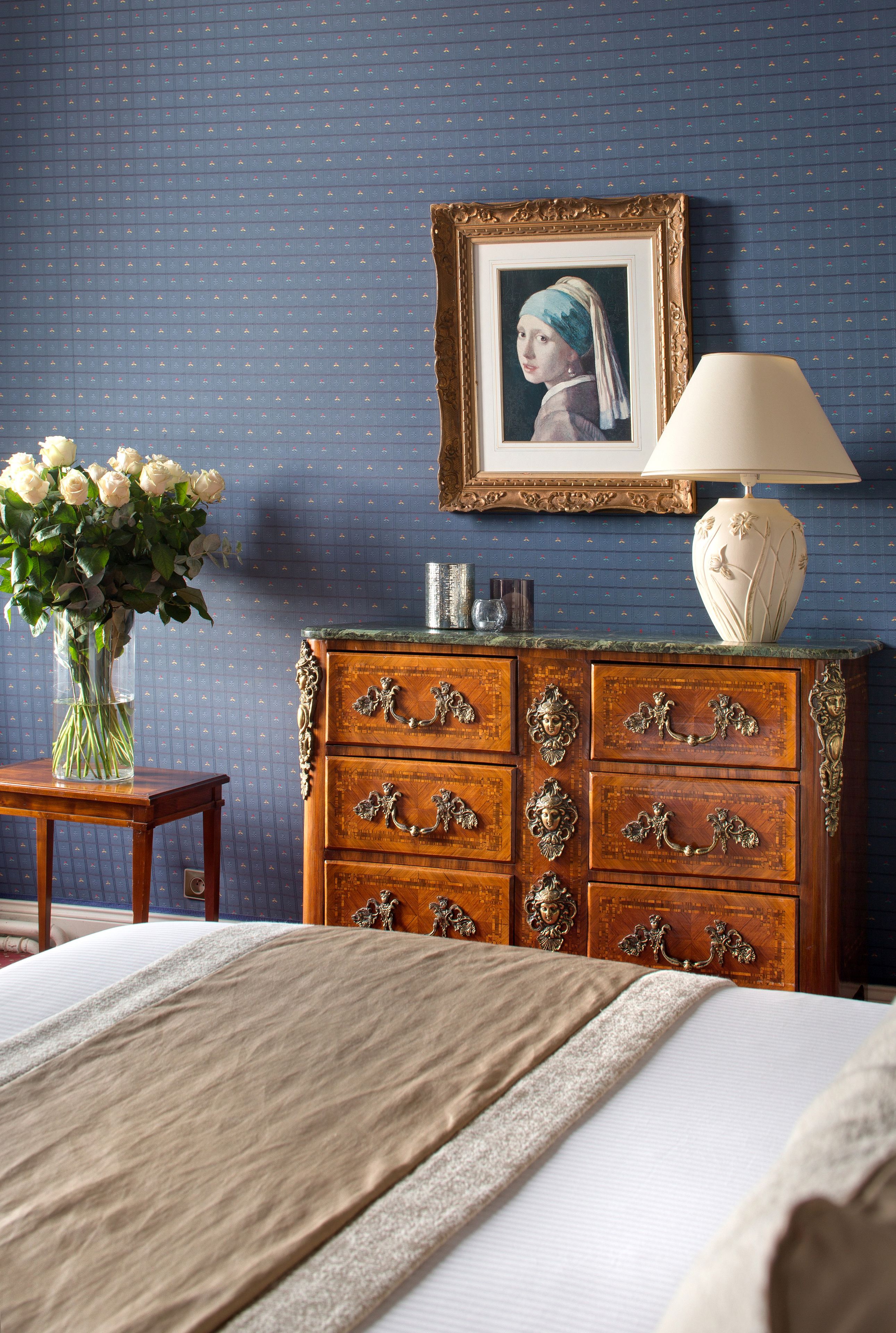 Un dormitorio con un aparador de madera, un cuadro en la pared, un jarrón de flores y una lámpara.