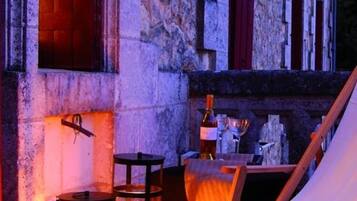 Un edificio de piedra con ambiente rústico, que presenta una mesa con una botella y vasos, una silla de madera y dos faroles.