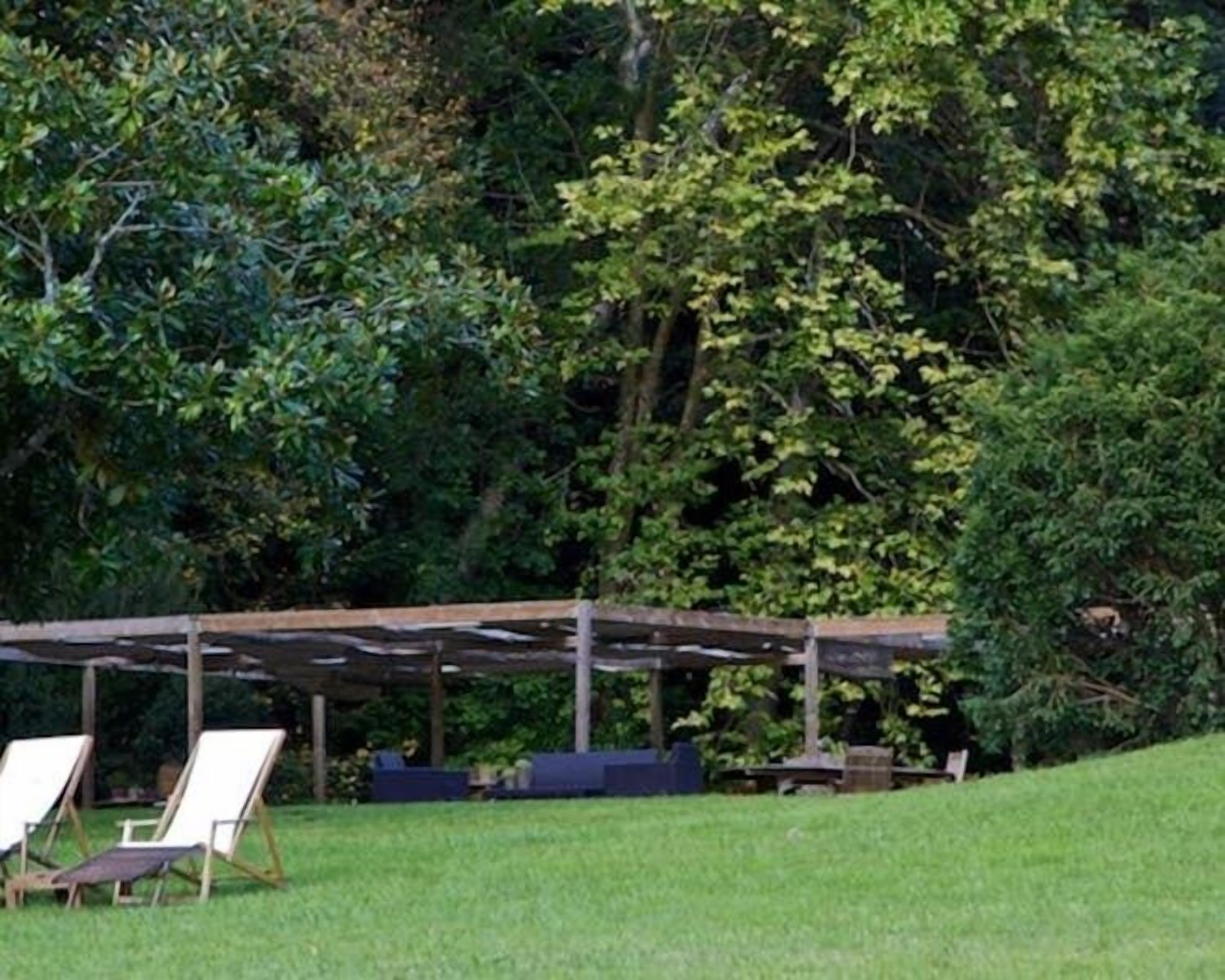 Zona salotto all'aperto coperta, con poltrone da giardino e un tavolo, immersa nel verde.
