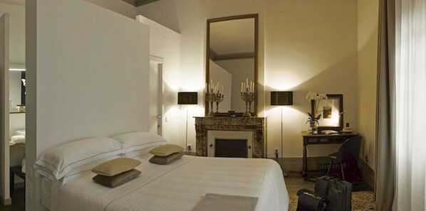 Una habitación de hotel con una cama grande, chimenea, un escritorio con silla y un espejo en la pared.