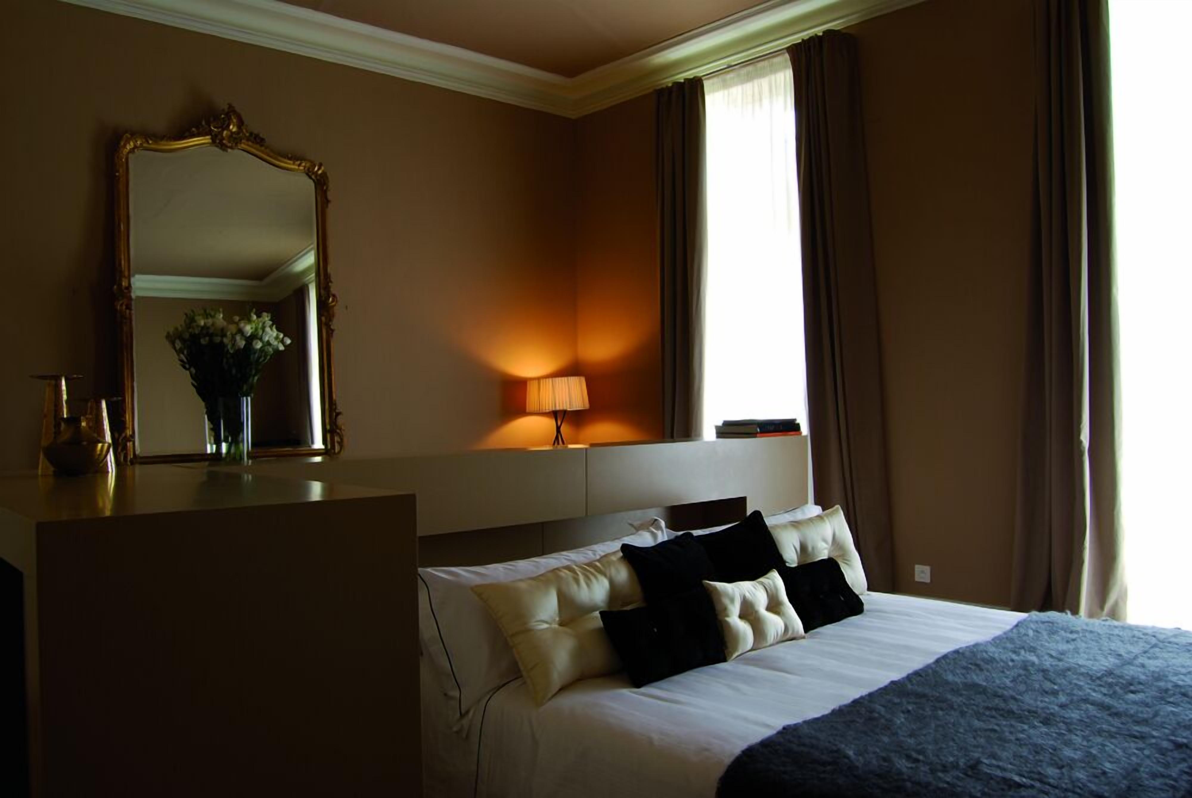 Een hotelkamer met een bed, een bureau, een spiegel, een lamp en een raam met gordijnen.