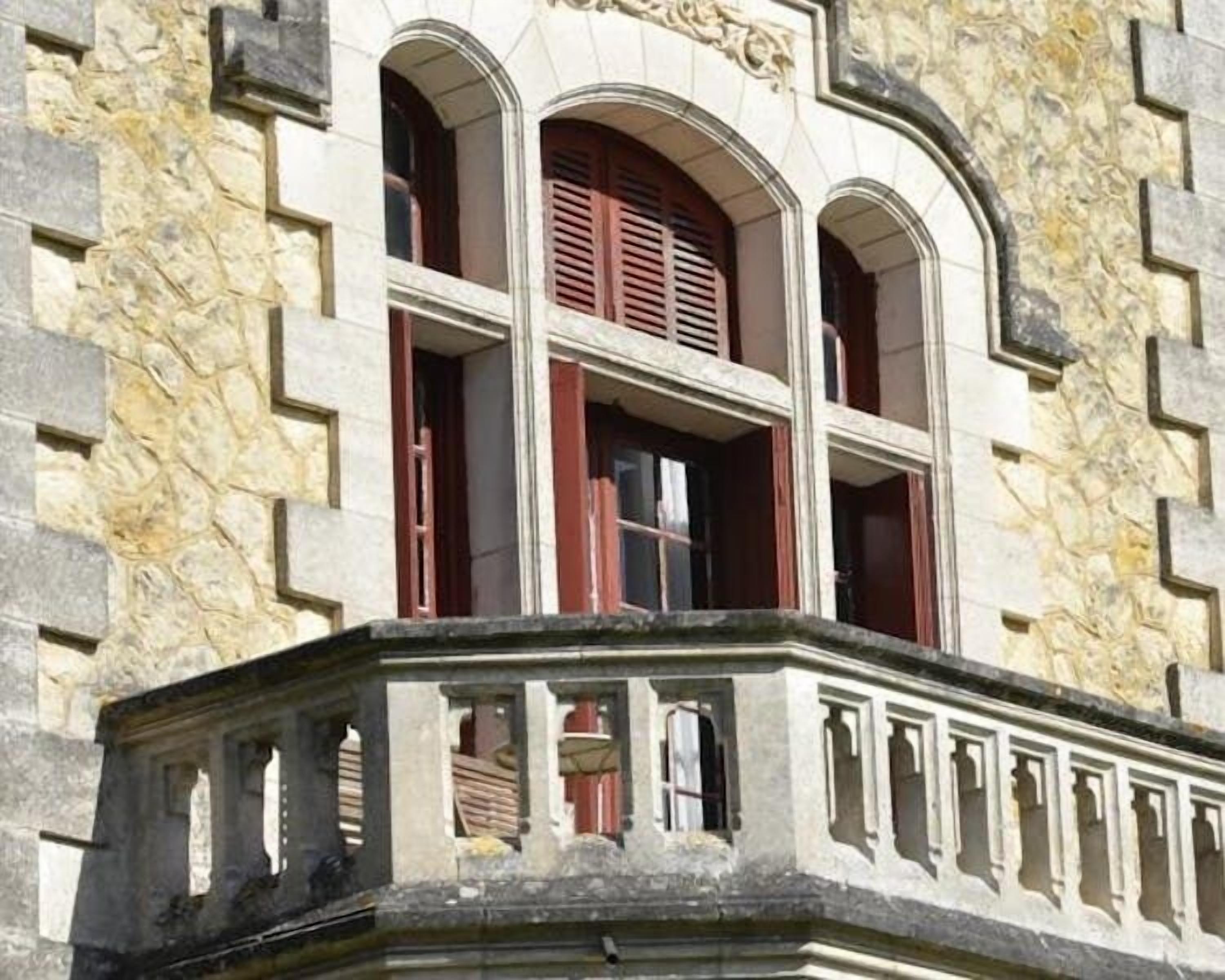 Un edificio con fachada de piedra, ventanas arqueadas y un balcón con barandillas.