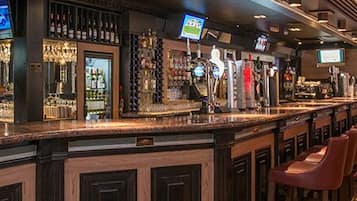 A bar area with a long counter, multiple taps, and a television screen.