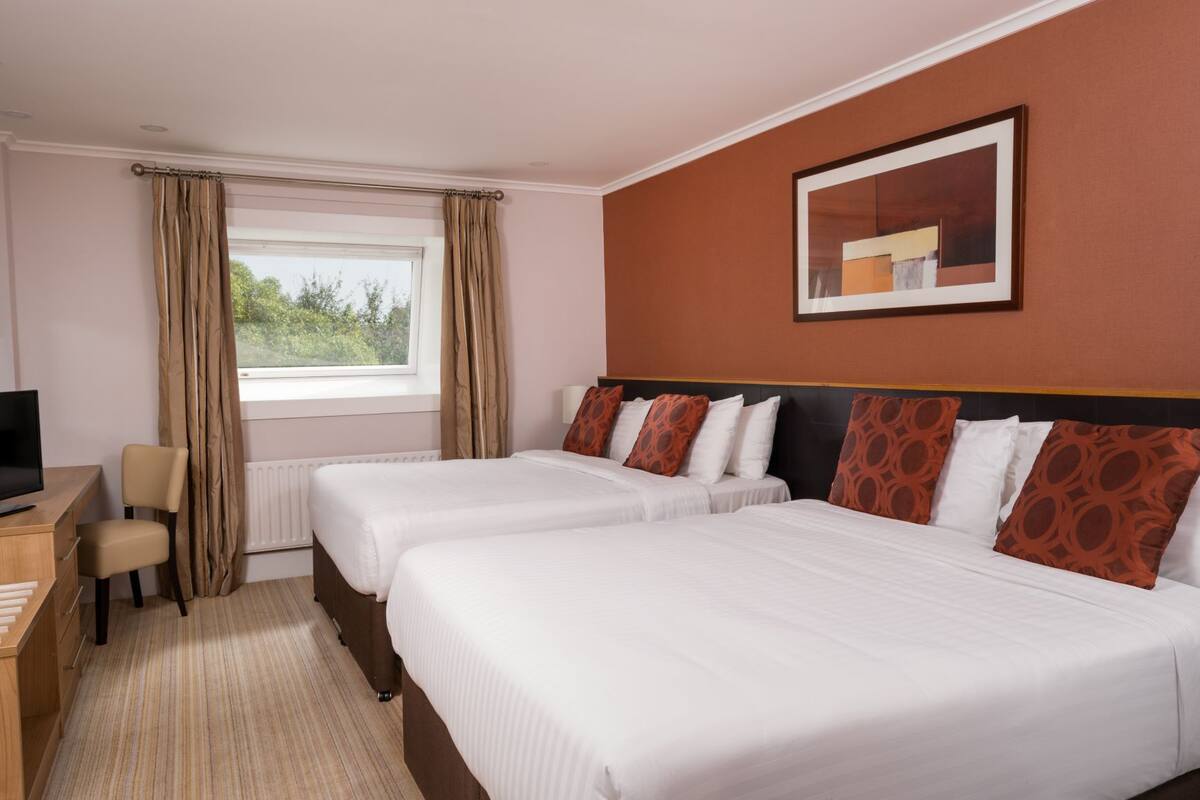 Habitación de hotel con dos camas, un escritorio, una silla, un televisor y una ventana con cortinas.