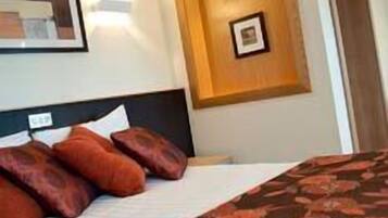 A hotel room with a bed, pillows, a framed picture on the wall, and a door.