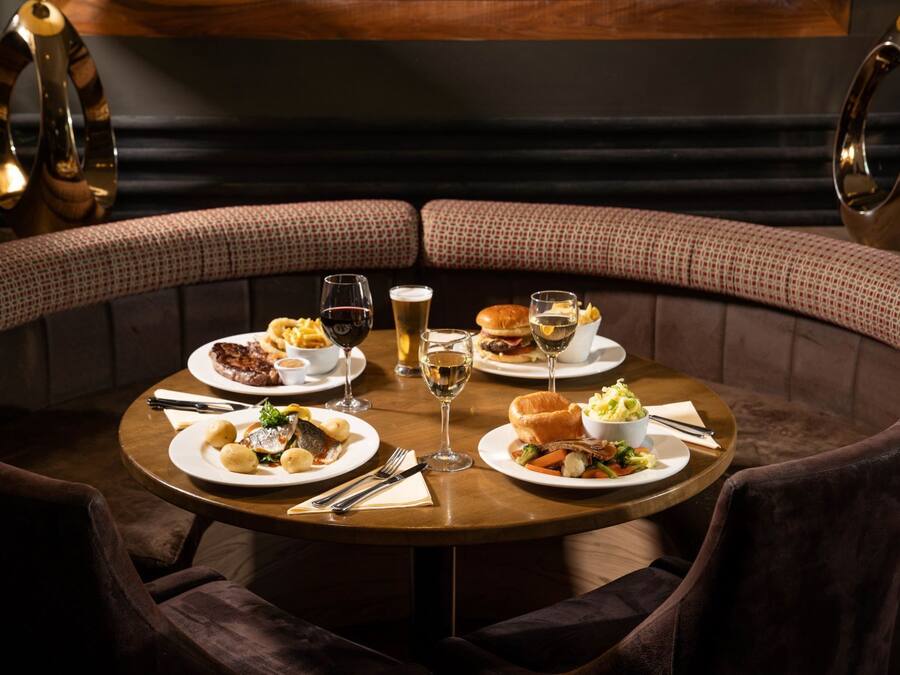 A round table with plates of food, glasses of wine, and a bowl of salad in a restaurant setting.