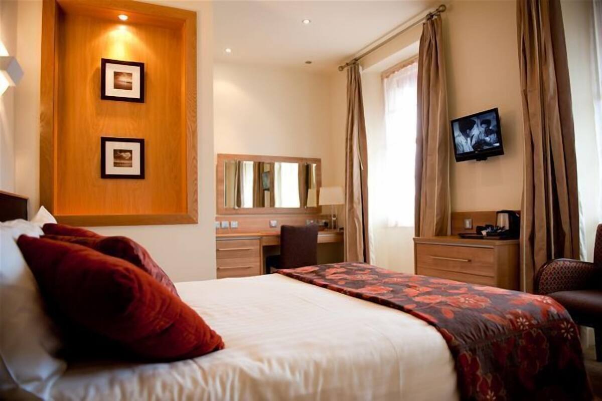 Una habitación de hotel con una cama, un escritorio, una silla, un televisor y un espejo.