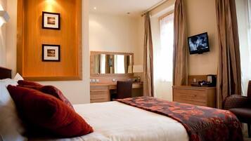 Una habitación de hotel con una cama, un escritorio, una silla, un televisor y un espejo.