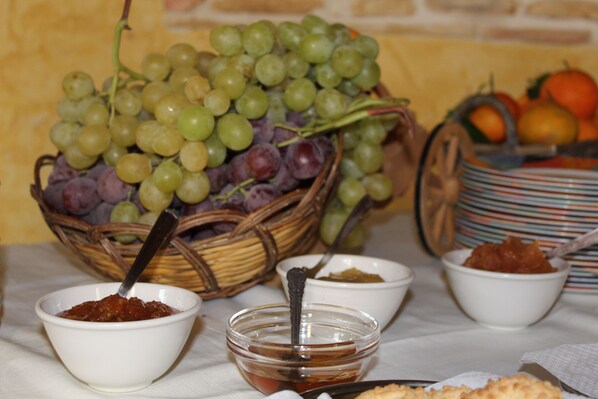 A table with a basket of grapes, bowls of jam, and a plate of biscuits. - Agriturismo La Maddalena (Acate)