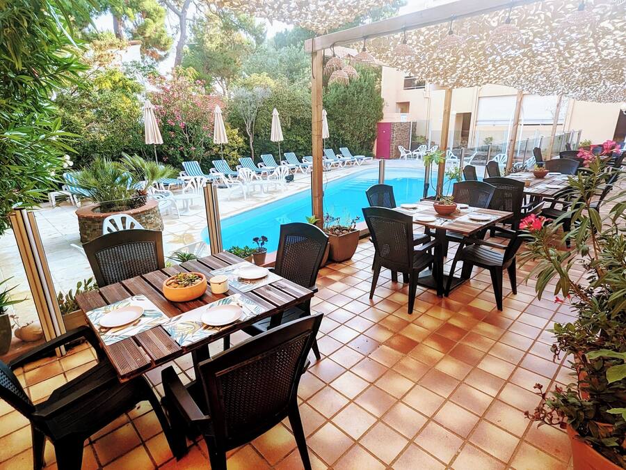 An outdoor dining area with tables and chairs, a pool, and surrounding greenery.