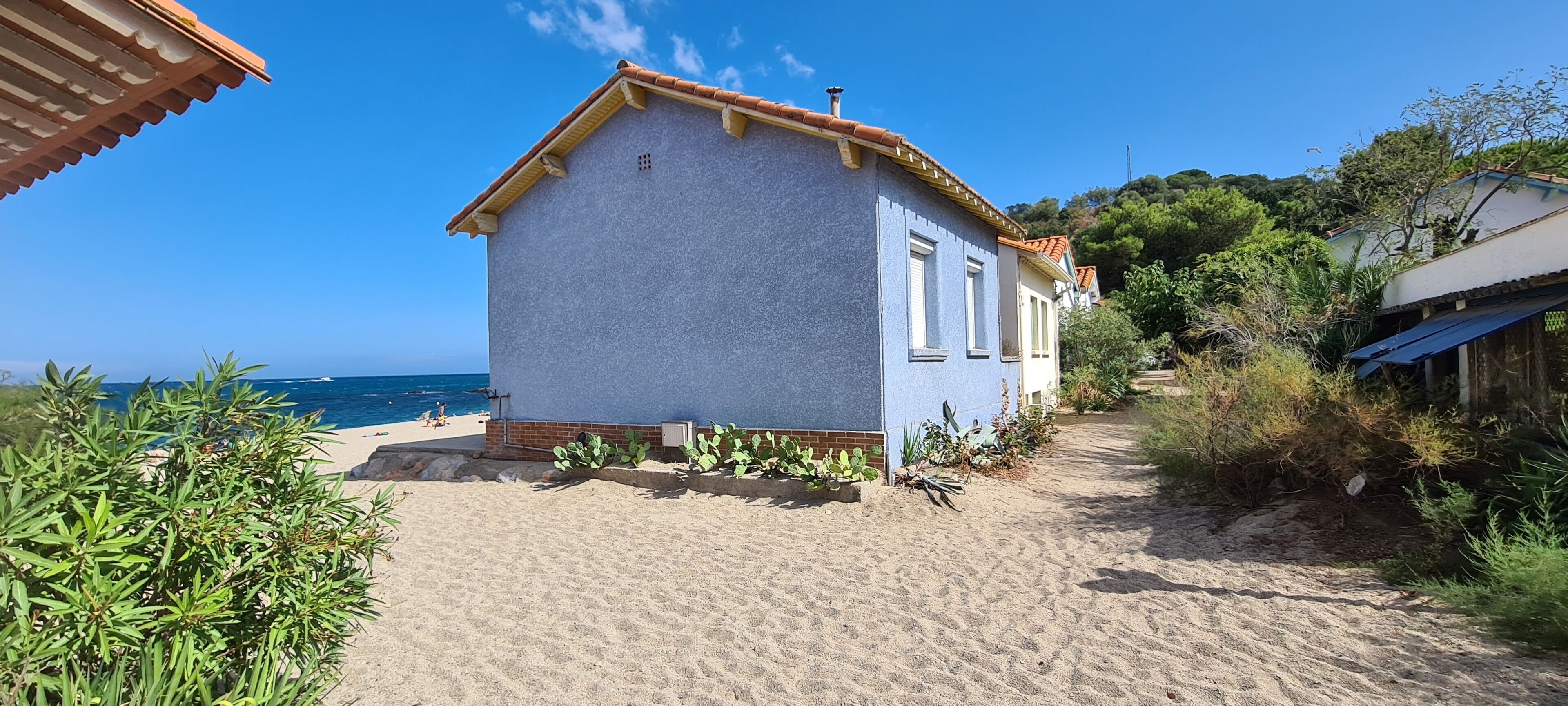 A beachfront property with a sandy path leading to a building with a tiled roof.