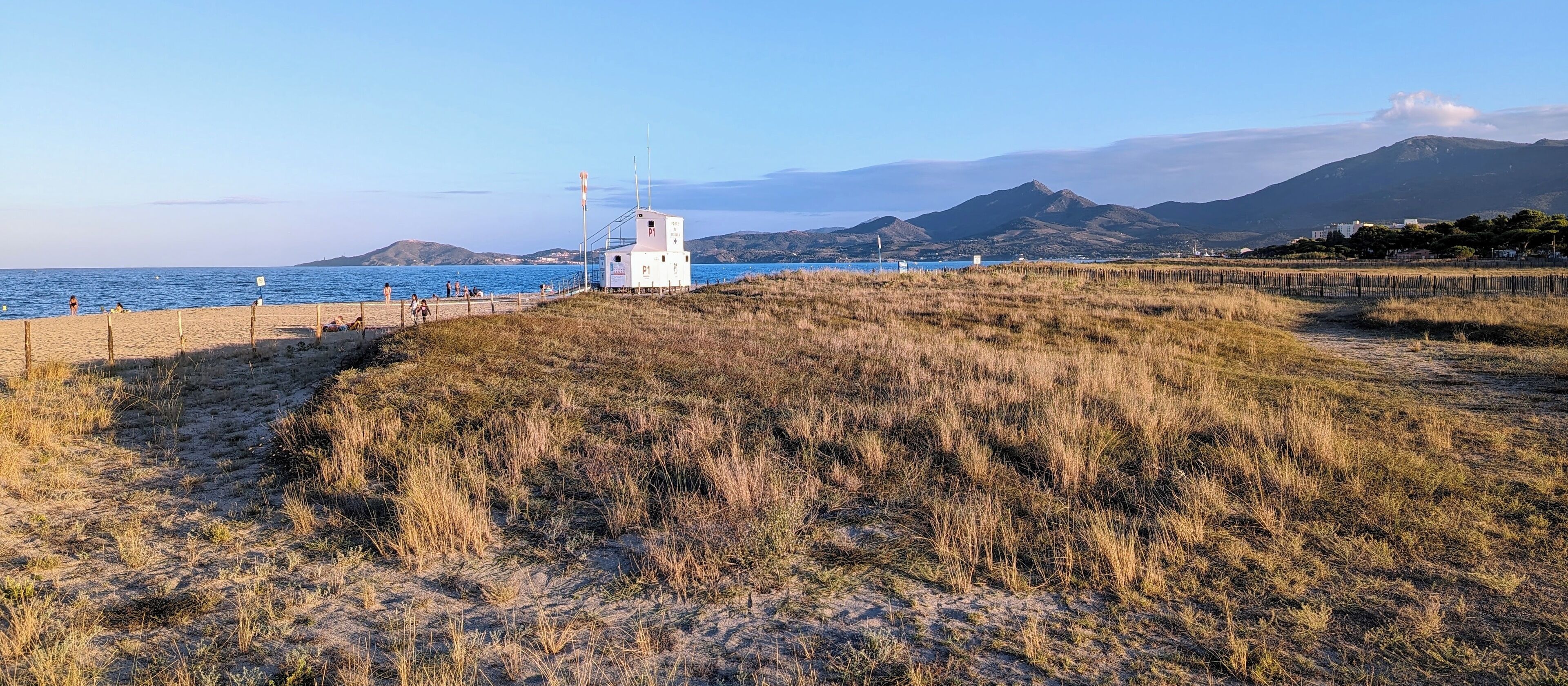 Un paisaje costero con un edificio blanco, posiblemente un faro, sobre una colina cubierta de hierba con vistas al mar.