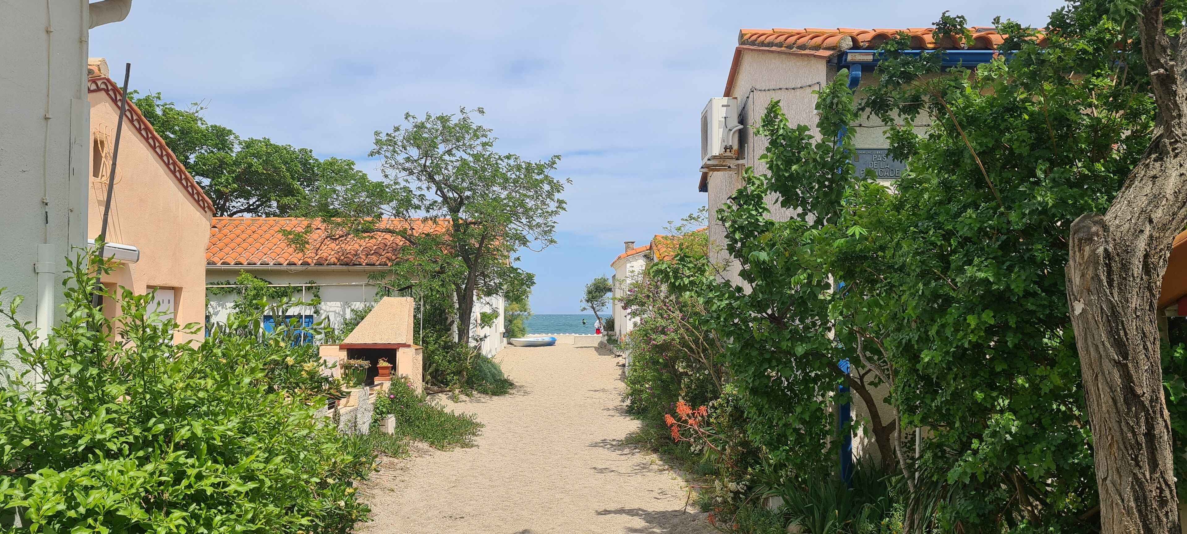A narrow pathway leading to a beach with buildings on either side, some with balconies overlooking the sea.