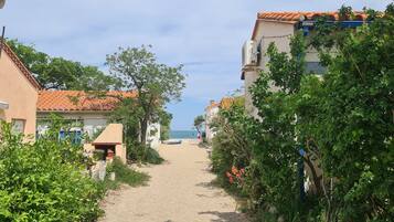 A narrow pathway leading to a beach with buildings on either side, some with balconies overlooking the sea.