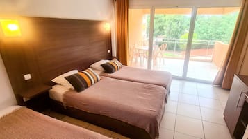 Habitación de hotel con dos camas, un balcón con sillas y una puerta corrediza de vidrio al exterior.
