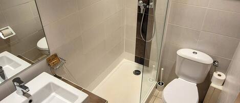 Een moderne badkamer met een douchecabine van glas, een witte wastafel en een toilet.