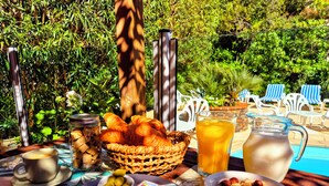 Una mesa de desayuno con cruasanes, un cuenco de fruta, una jarra de jugo y un tazón de cereal.