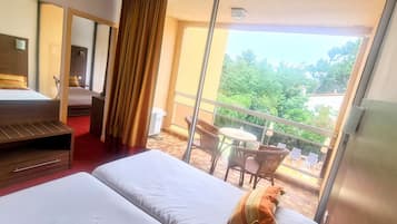 A hotel room with a bed, a desk, a chair, and a balcony with outdoor furniture.