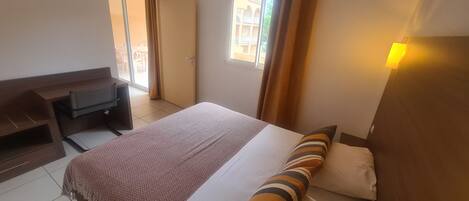 A hotel room with a bed, a desk, a chair, and a window with curtains.