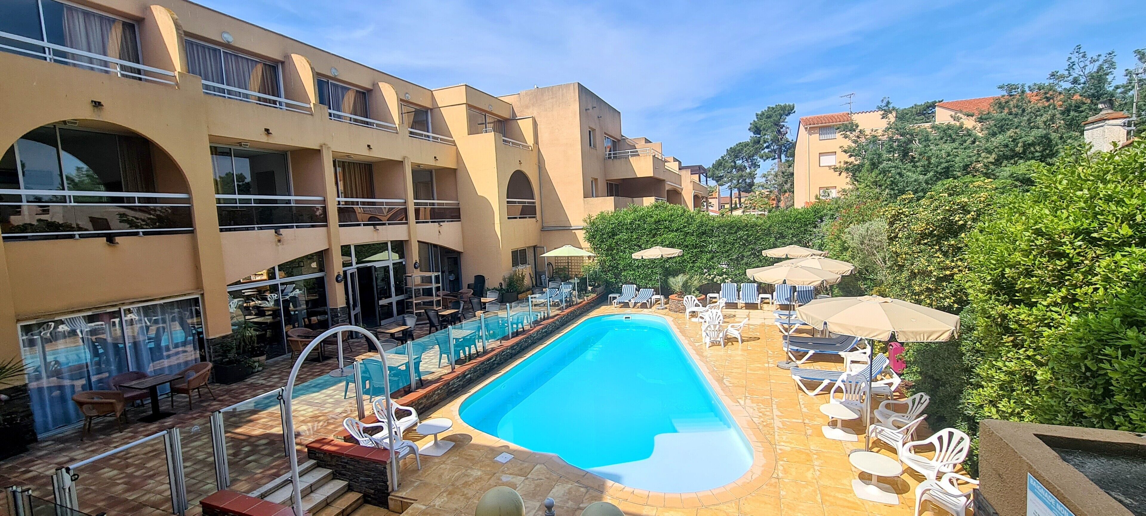 A hotel with a swimming pool, outdoor seating, and a view of the surrounding buildings.