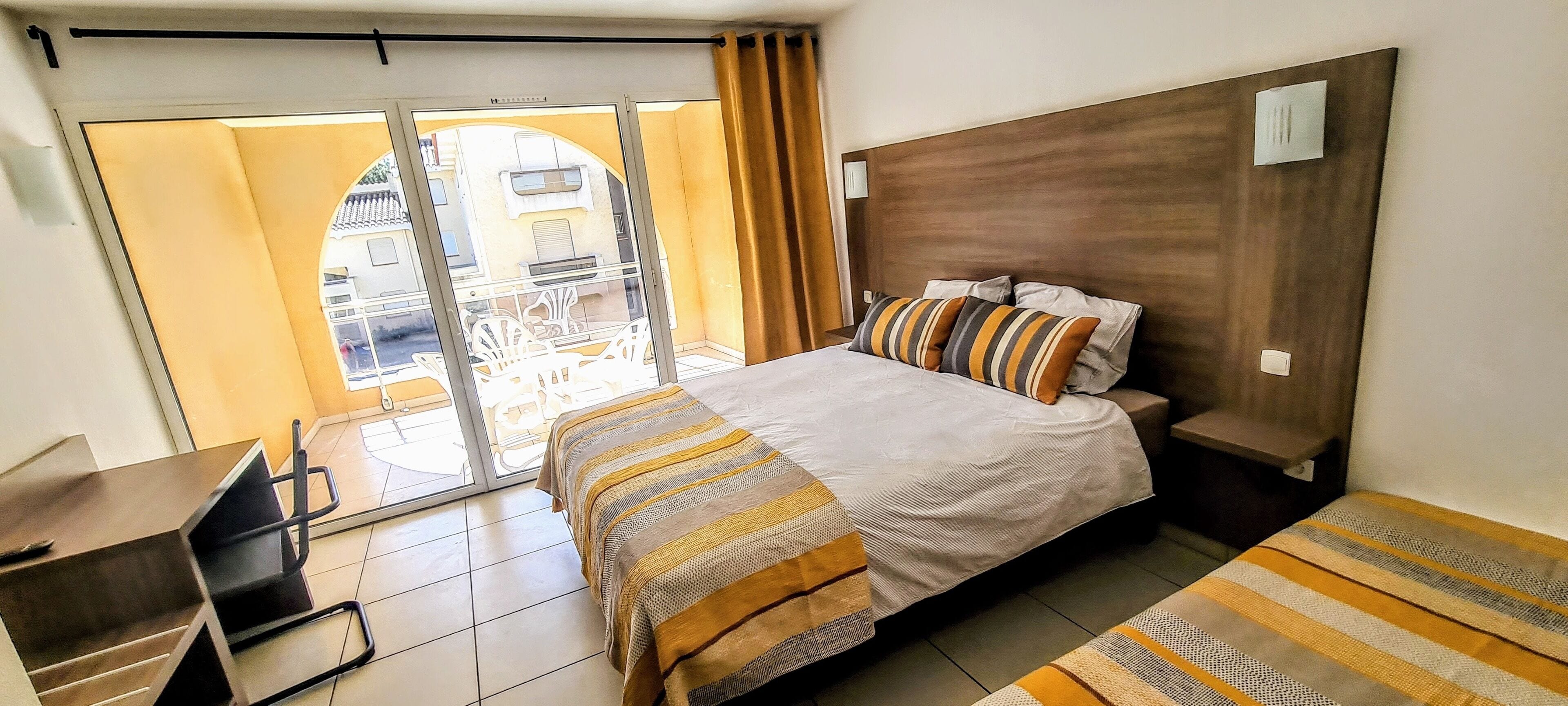 A hotel room with a bed, a desk, a chair, and a view through a sliding door to the outside.