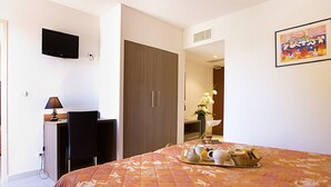 Habitación de hotel con cama, escritorio y silla, televisor montado en la pared y un cuadro.