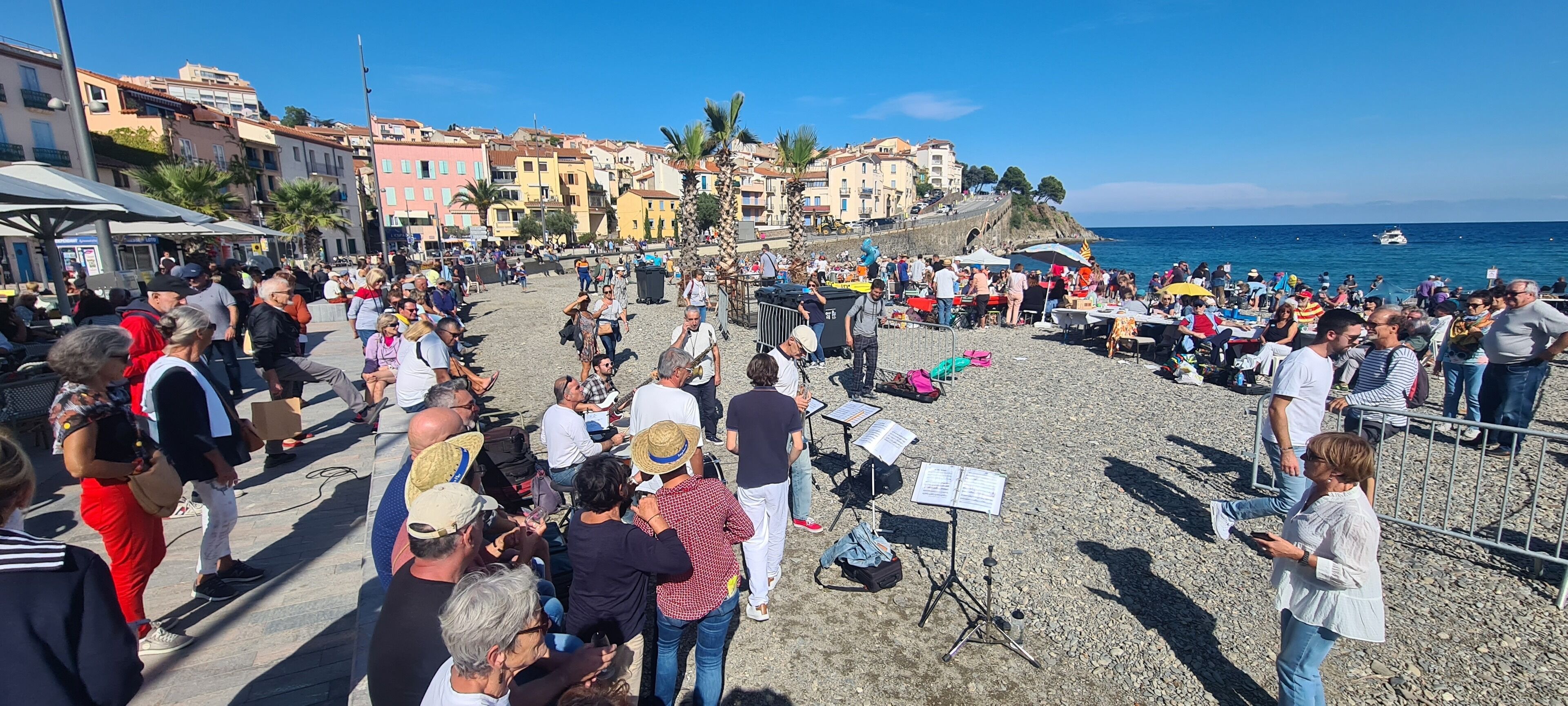 Uma praia movimentada com pessoas, suportes para instrumentos musicais e um palco.