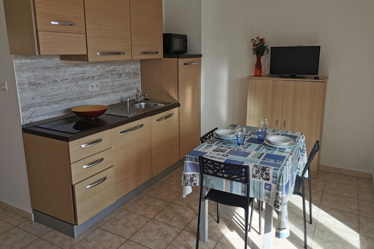 Une cuisine compacte dotée de meubles en bois, d’un four à micro-ondes, d’un évier et d’un coin repas avec une table mise pour deux personnes.