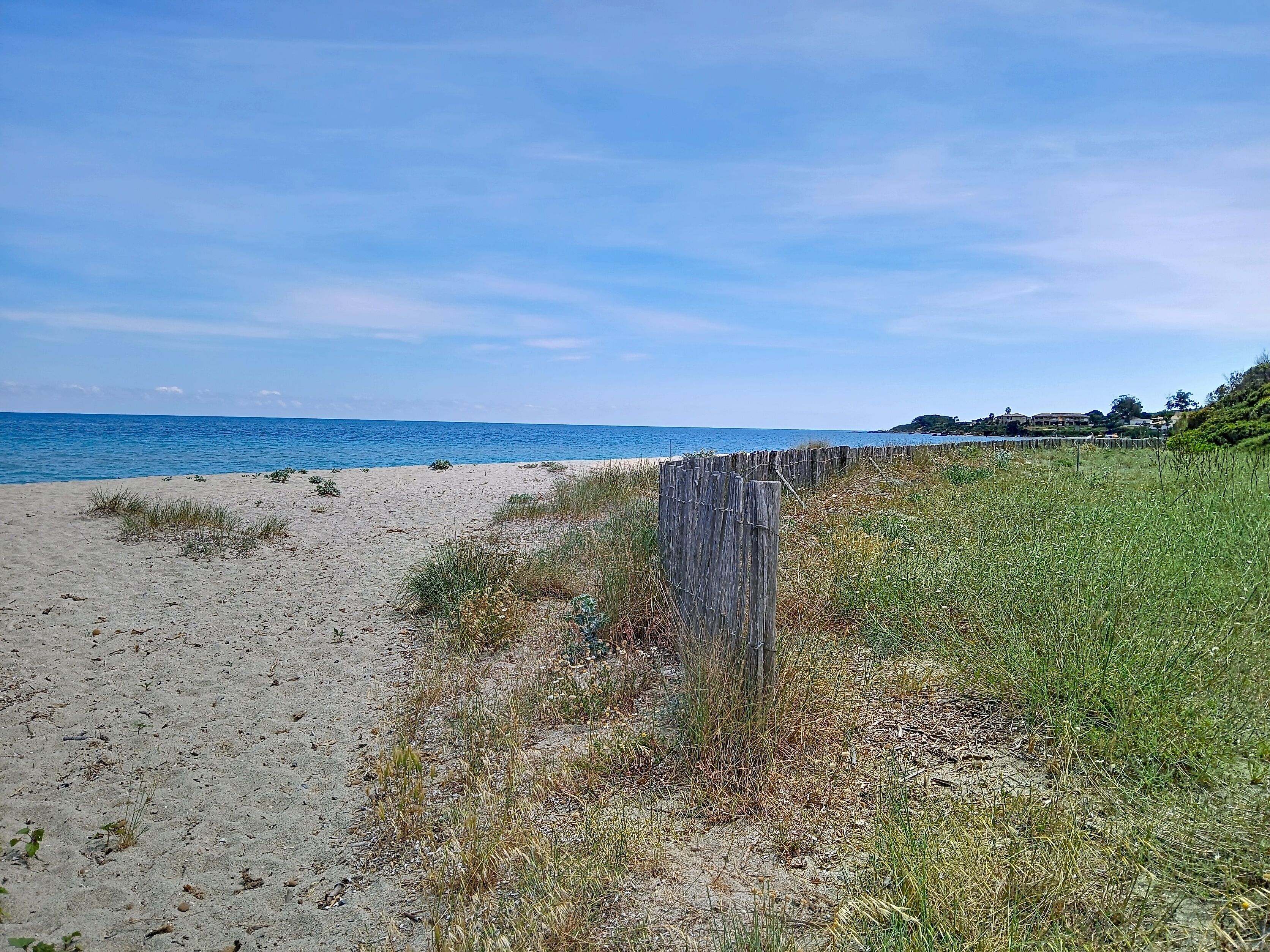A beach with a wooden fence, sandy shore, and a distant building.