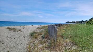 Una playa con una cerca de madera, orilla arenosa y un edificio a lo lejos.