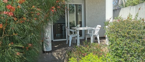 A patio area with a table and chairs, surrounded by greenery and a building entrance.