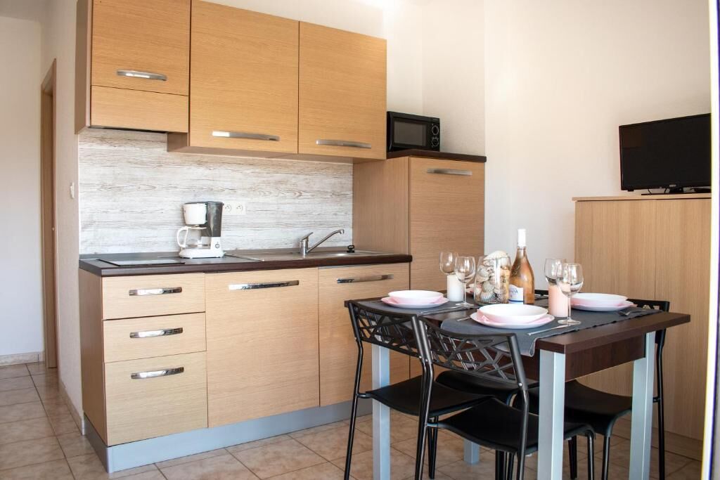 A compact kitchen with wooden cabinets, a microwave, a coffee maker, and a dining area with a table set for two.