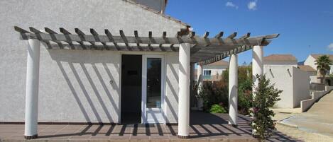 Un bâtiment doté d’un patio couvert, d’une porte et d’un petit arbre.