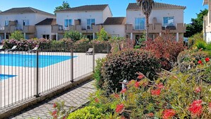 A residential building with a swimming pool, surrounded by lush greenery and a clear blue sky.