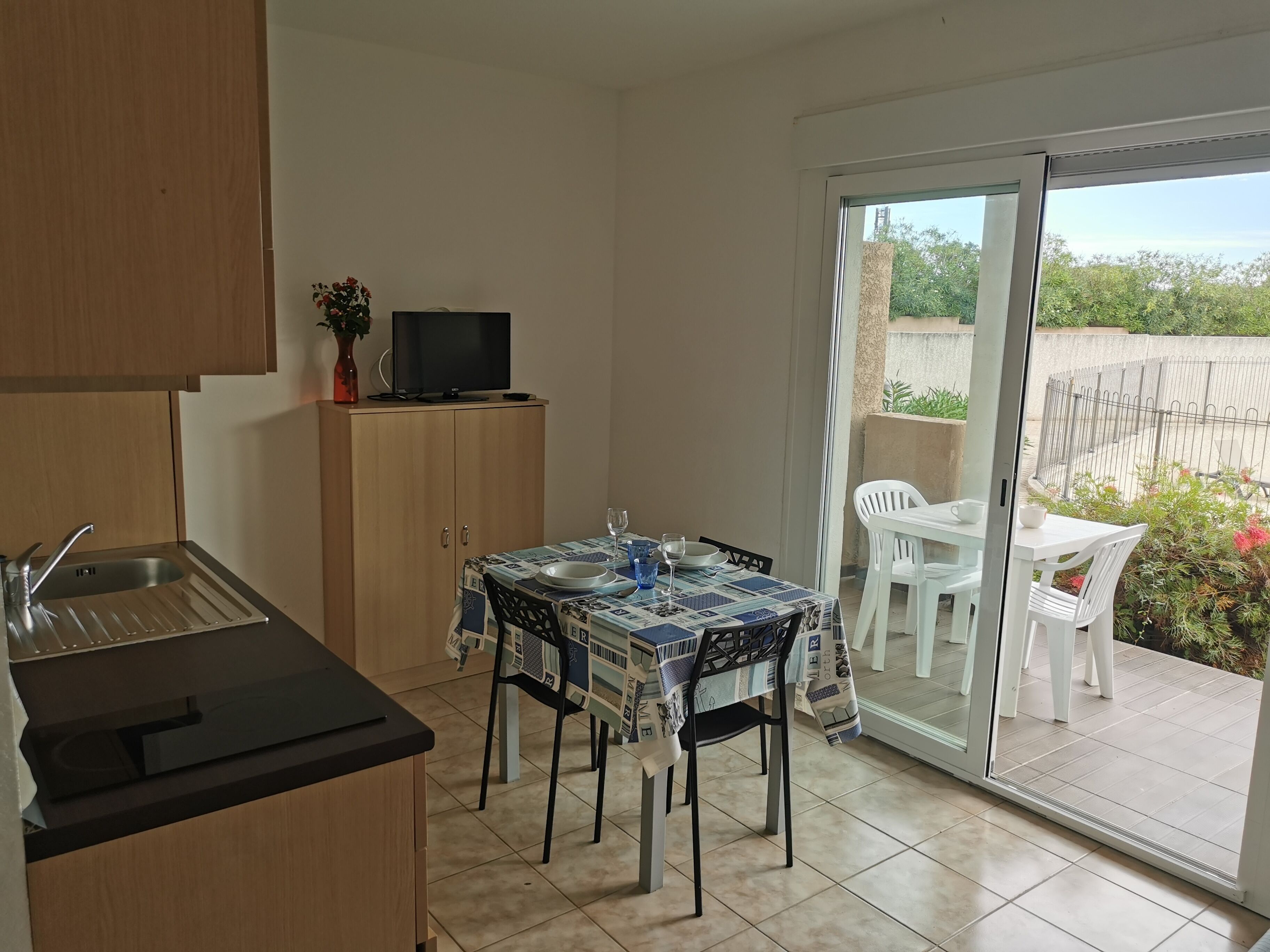A compact kitchen with a dining area, a TV on a cabinet, and a sliding glass door leading to an outdoor patio.
