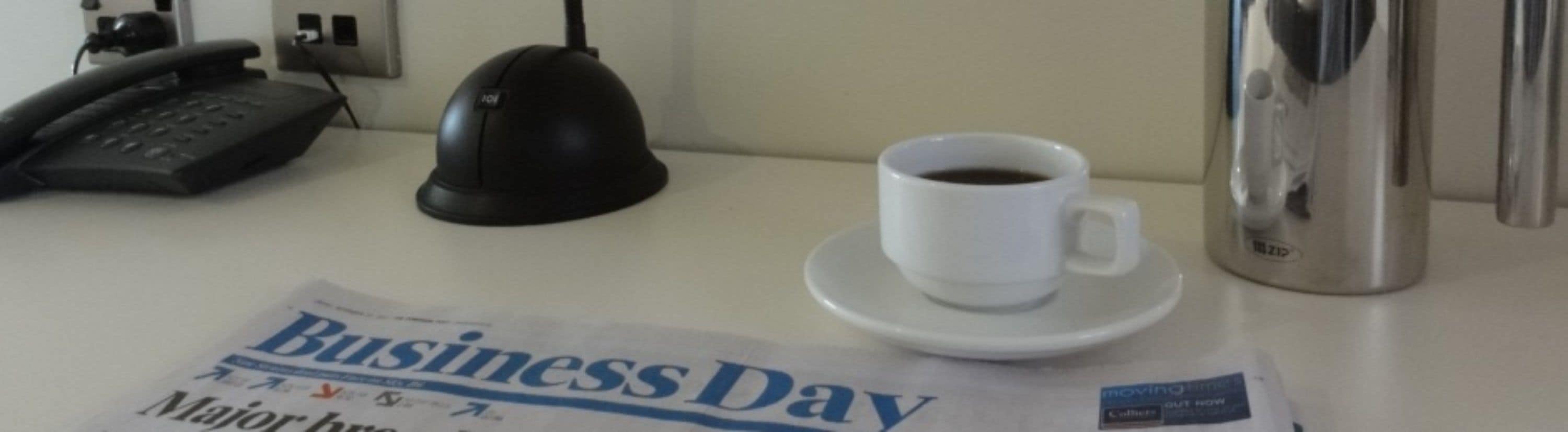 A business newspaper on a table with a coffee cup and a telephone.