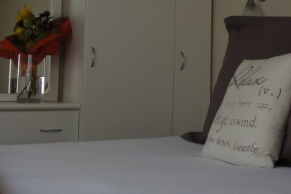 A bedroom with a bed, a nightstand, a mirror, and a vase with flowers.