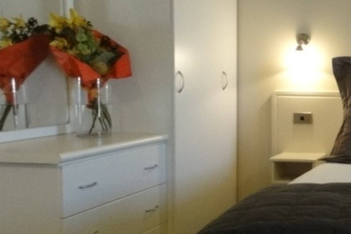 A bedroom with a bed, two bedside tables, a nightstand, and a wall-mounted light fixture.
