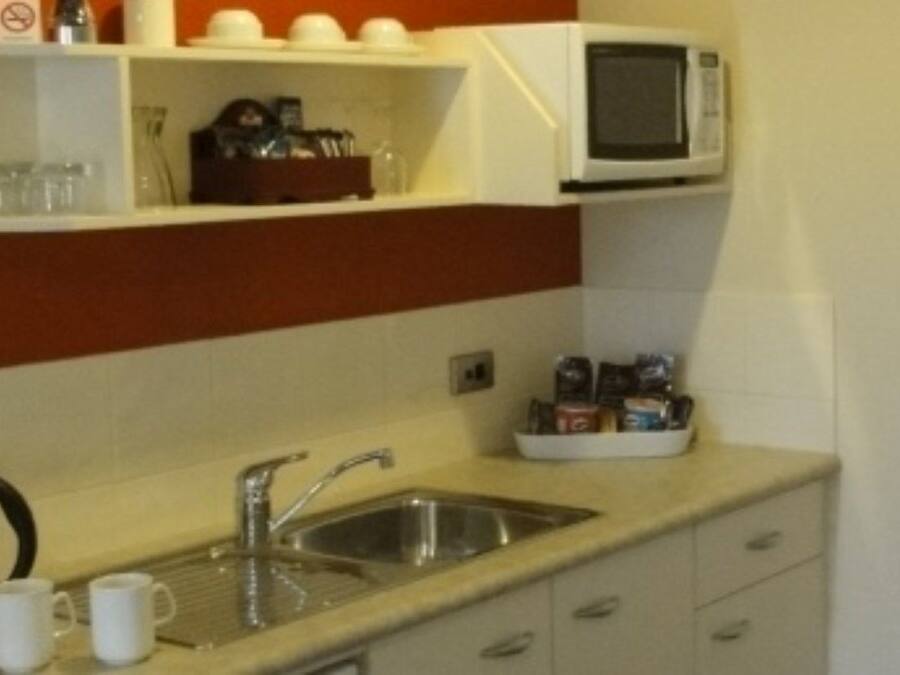 A small kitchenette with a sink, kettle, microwave, and storage cabinets.
