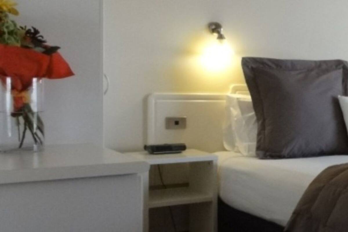 A hotel room with a bed, bedside table, lamp, and a chair.