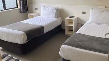 A hotel room with two single beds, a small table, a chair, and a window with curtains.