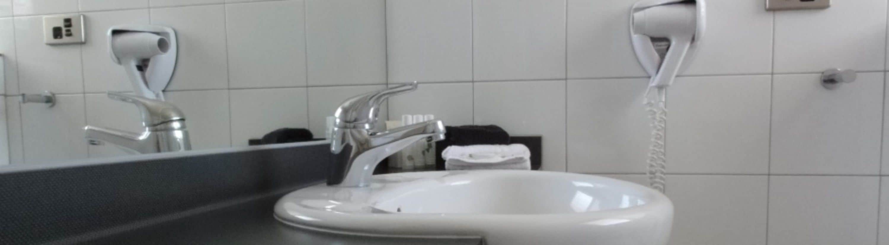 Ein Badezimmer mit einem weißen Waschbecken, einem Spiegel und einem an der Wand befestigten Fön.