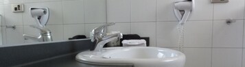 Un baño con lavamanos blanco, espejo y secador de pelo montado en la pared.