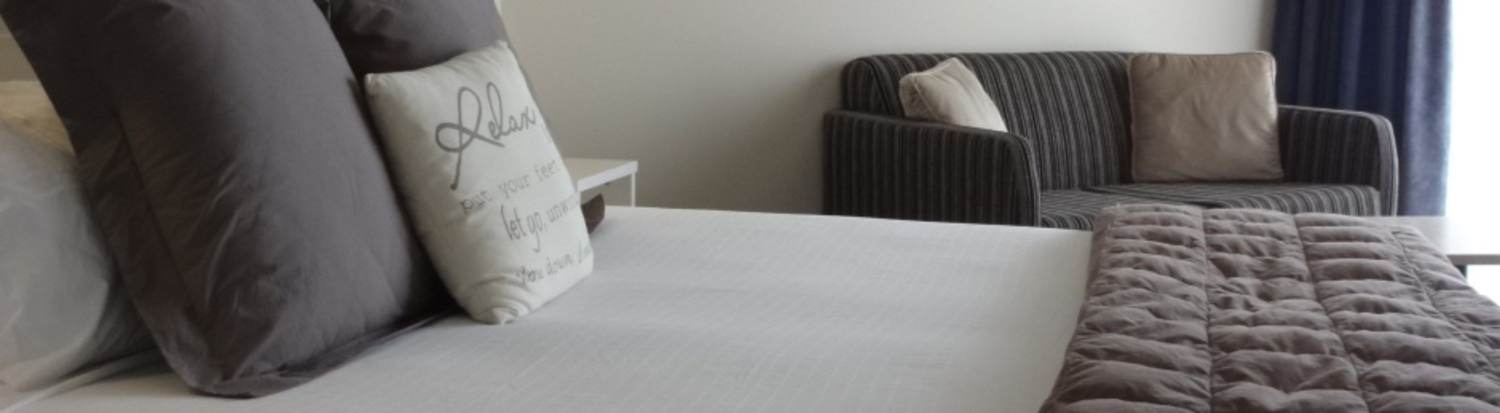 A hotel room with a bed, a grey sofa, and a white nightstand.
